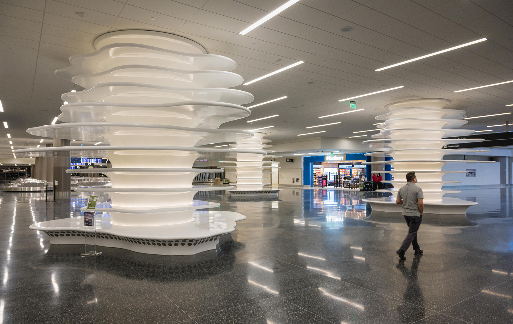 man walking through airport concourse with shops and art displays