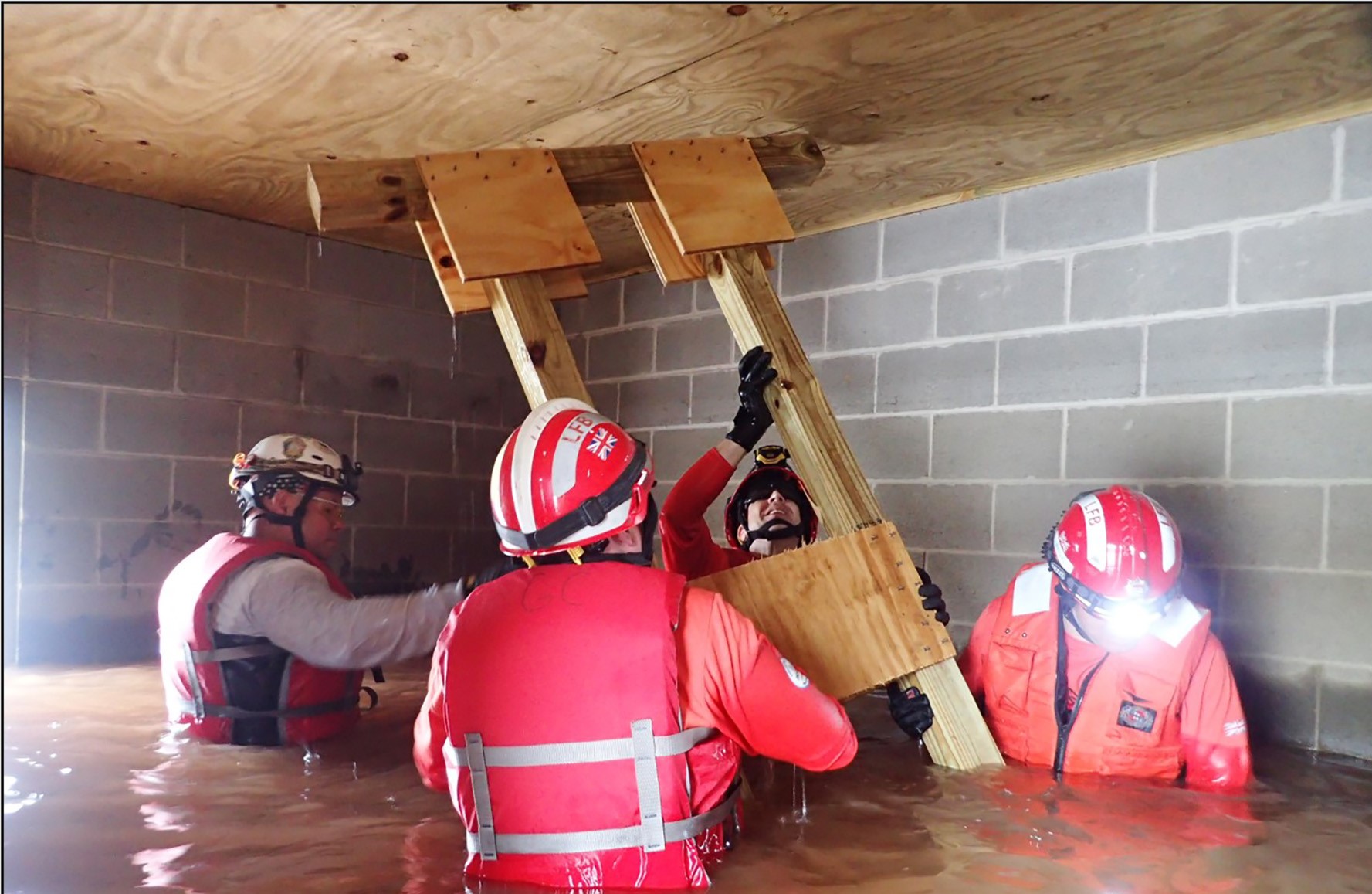 men standing in waist-deep water holding ladder. They are wearing safety vests, and helmets, and gloves