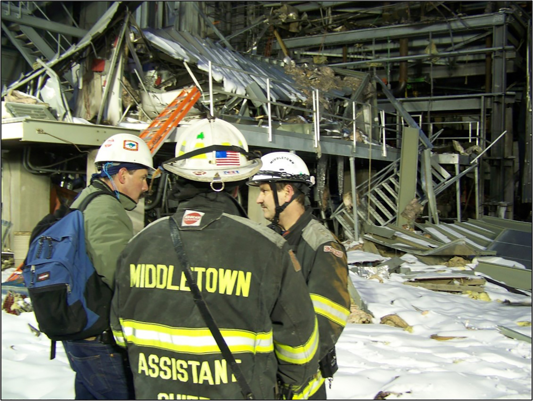men in rescue gear standing in front of a destroyed building