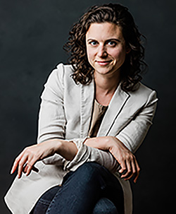 woman in beige jacket and black pants with short brown hair smiling