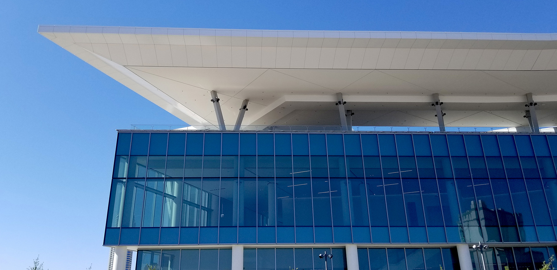 Multistory building with tall glass windows and white roof supported by V-shaped beams.