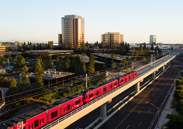 red train moves along tracks amidst a city scape in San Diego