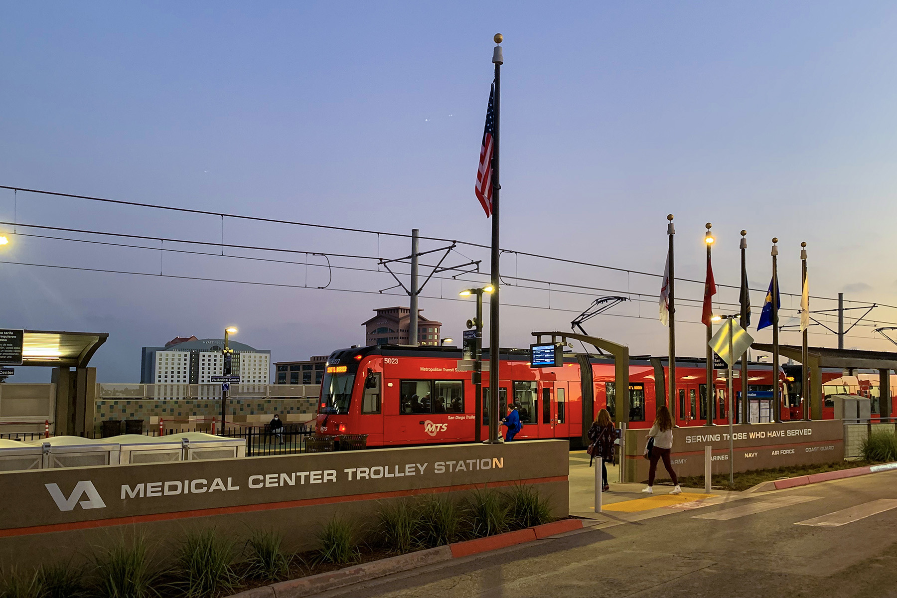 Train stopped at a trolley station. People are walking toward the train to board it.