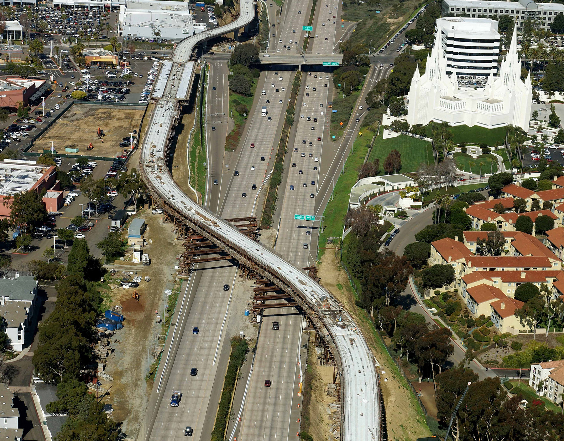 Aerial photograph of construction of a section of the trolley line that runs over a highway. Houses and other buildings dot the landscape