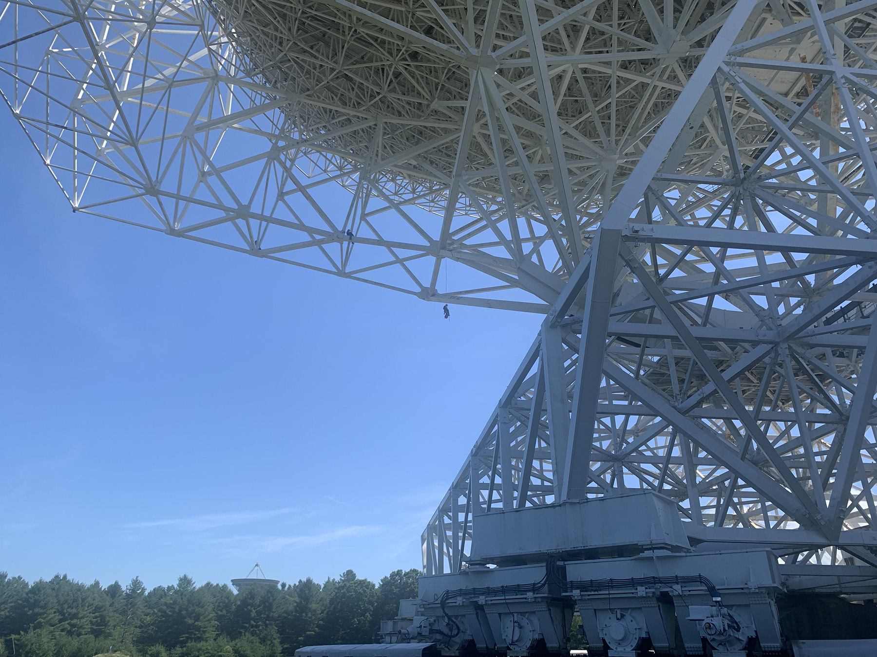 person hanging off the side of a telescope. He is tethered to it by a long wire.