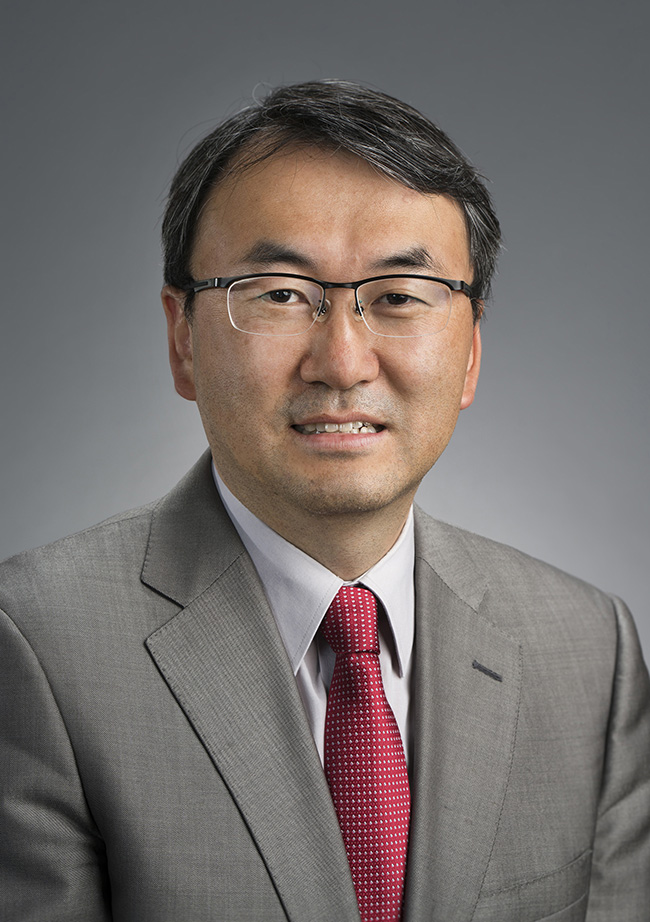 man in a grey suit, blue shirt, maroon tie wearing glasses