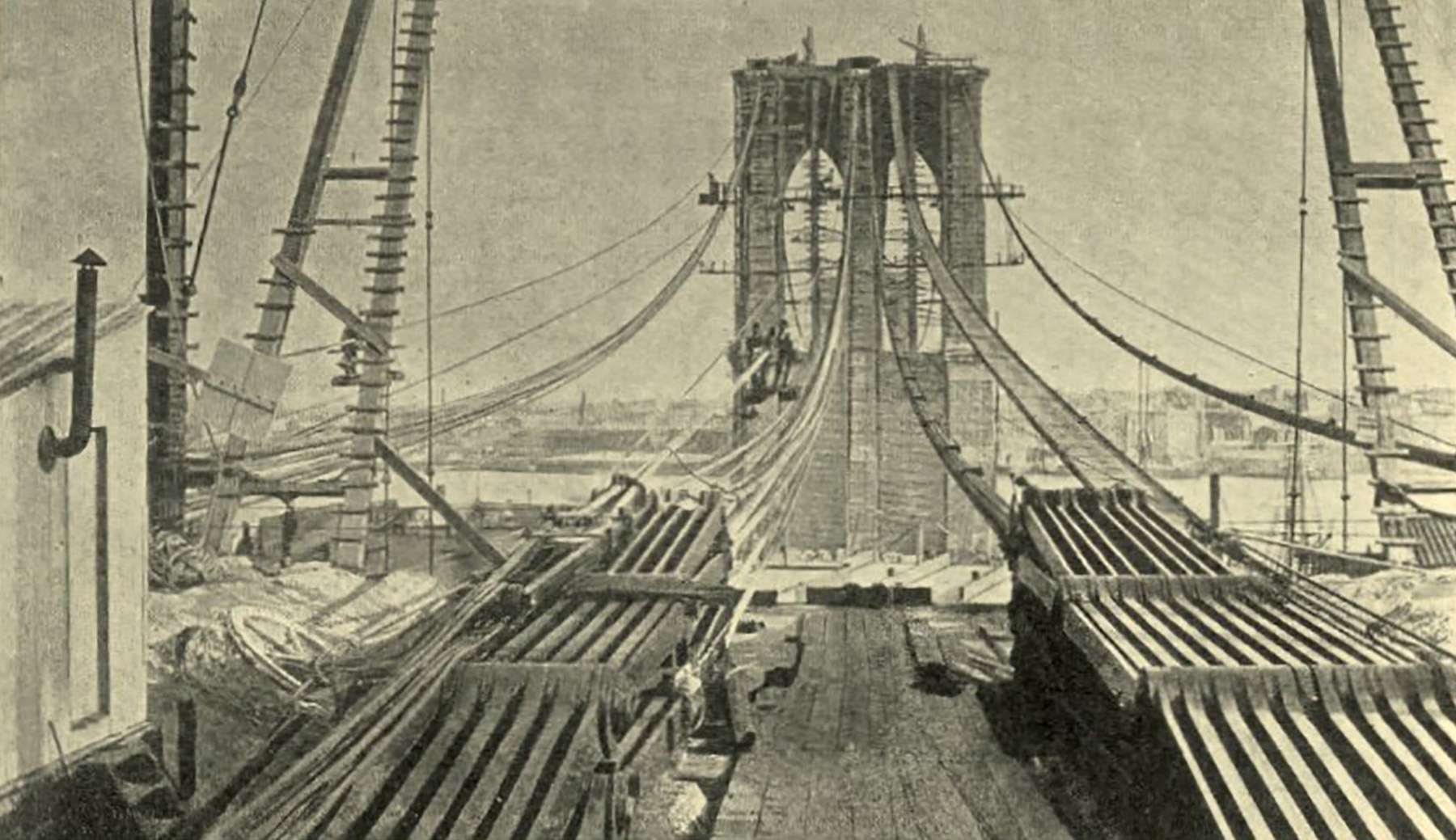 Black and white photograph of the Brooklyn Bridge showing it under construction. The laying of the cables is pictured.