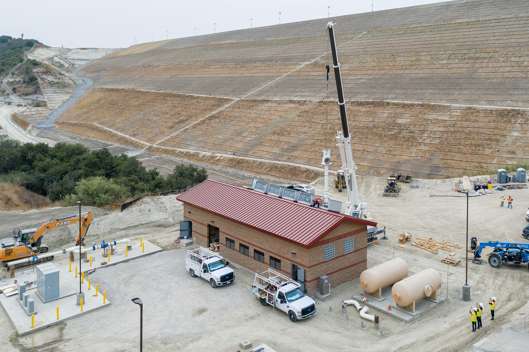 Small brown building with red roof surrounded by tanks, trucks, and equipment