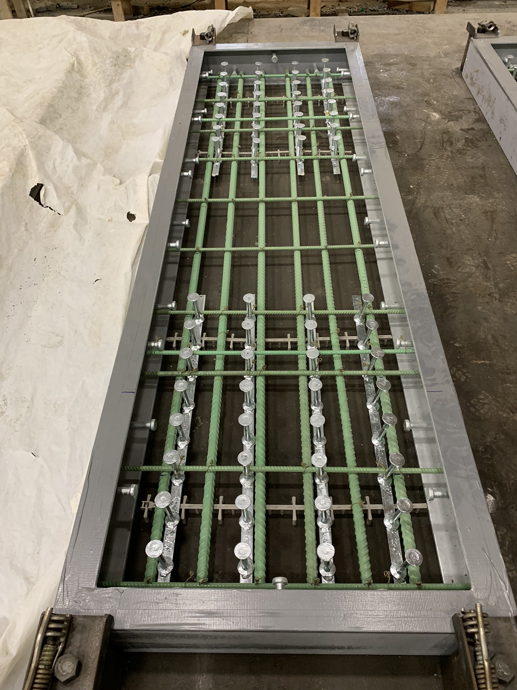  Long rectangular metal trench with green crisscrossing bars. This is a sewer trench.