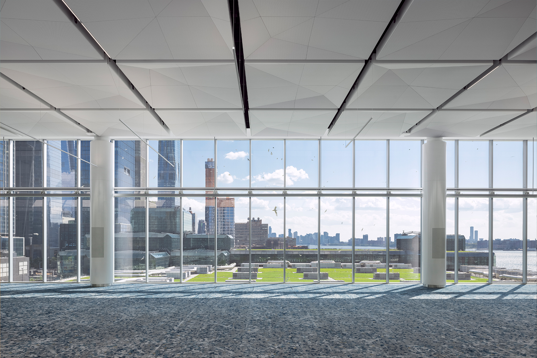 Large multilevel room with floor-to-ceiling glass panes that overlook a roof with grass