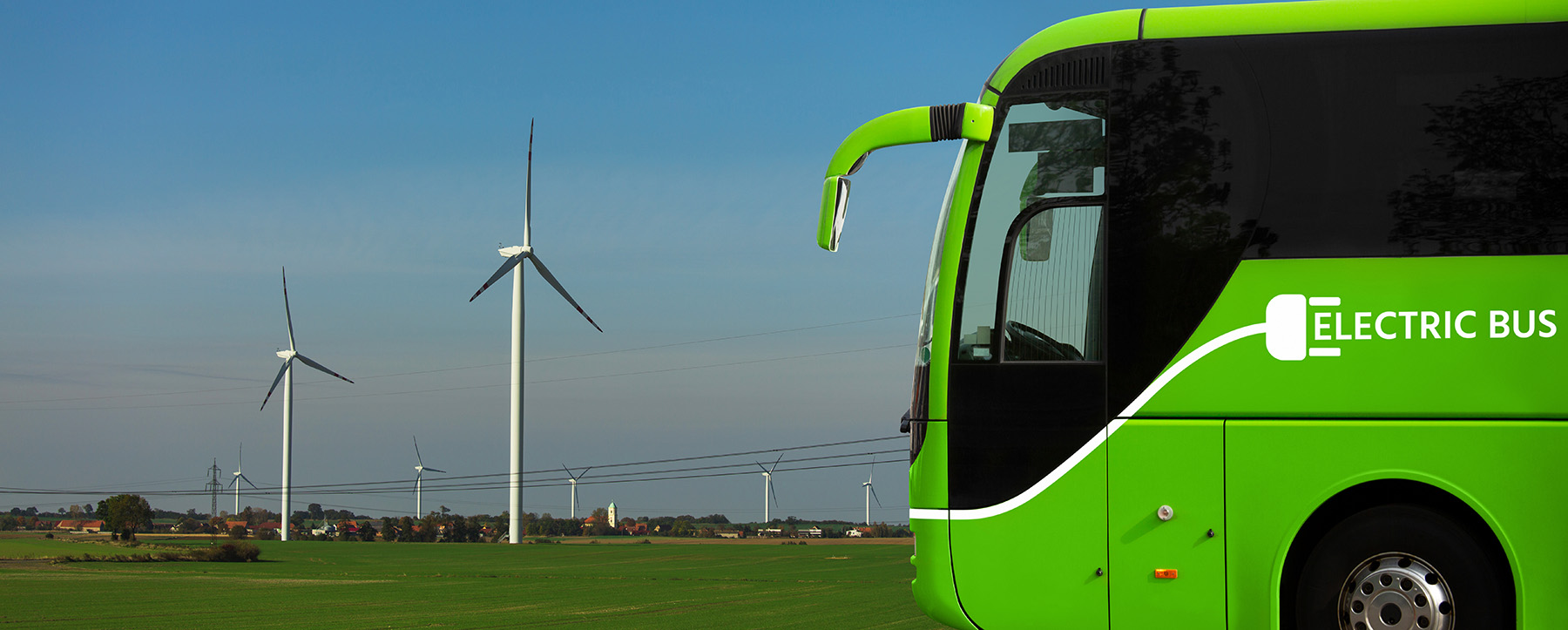 Green bus with white writing on it. in the background are windmills and power lines
