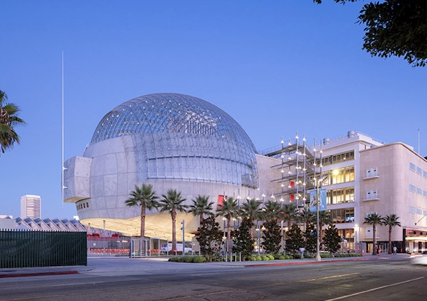 Large round structure with concrete base topped by a spherical glass roof. This building is connected by stairs to a multilevel building.