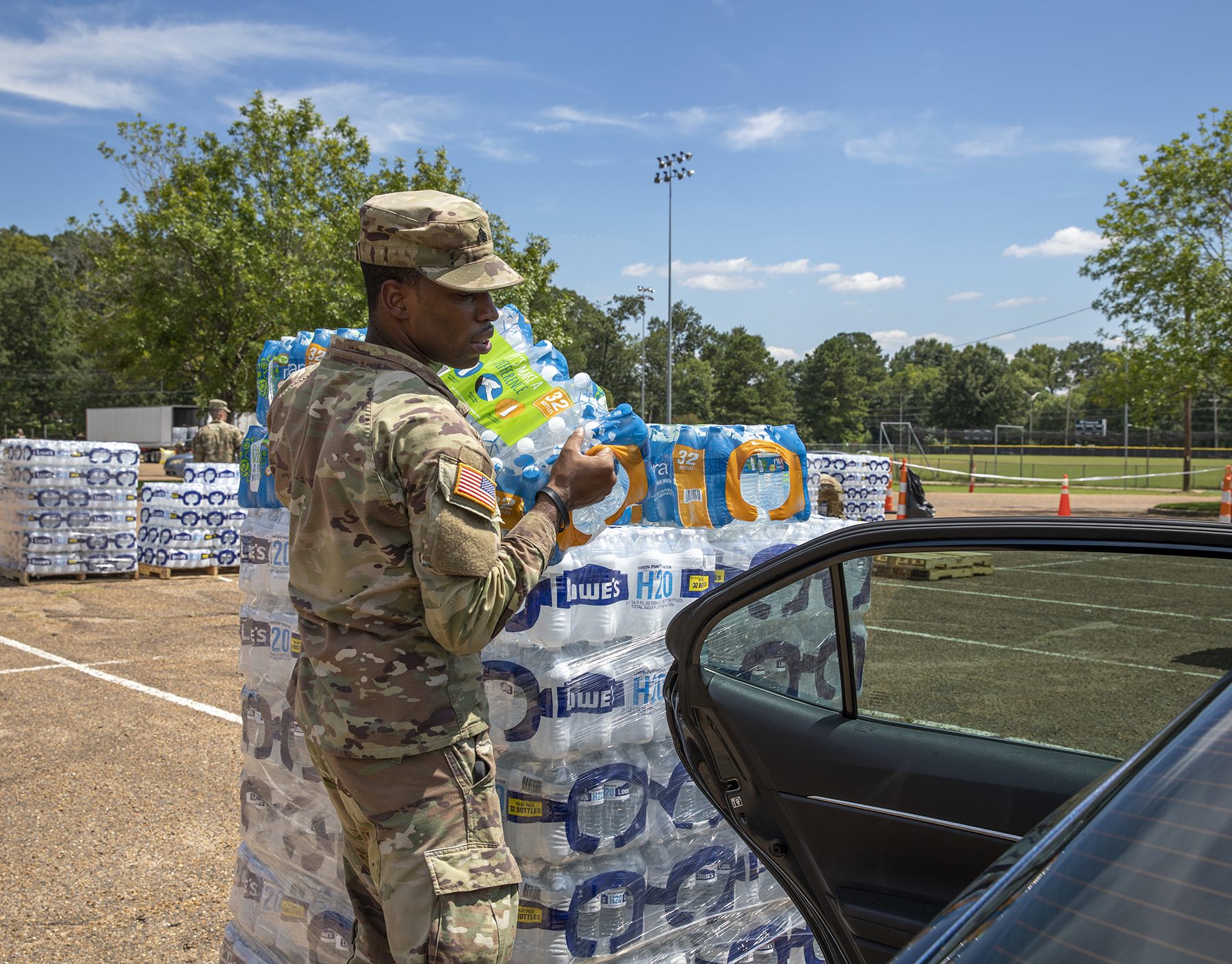 A soldier with 66th Troop Command, Mississippi Army National Guard, puts water in the backseat of a person's car at the Smith-Wills Stadium in Jackson, Mississippi, Sept. 1, 2022. Nearly 600 Mississippi National Guardsmen were set up across seven sites throughout Jackson for residents to collect bottled water and non-potable water from water trucks to help relieve some effects of the Jackson water crisis. (U.S. Army National Guard photo by Staff Sgt. Connie Jones, https://www.flickr.com/photos/thenationalguard/52329354023/ s)