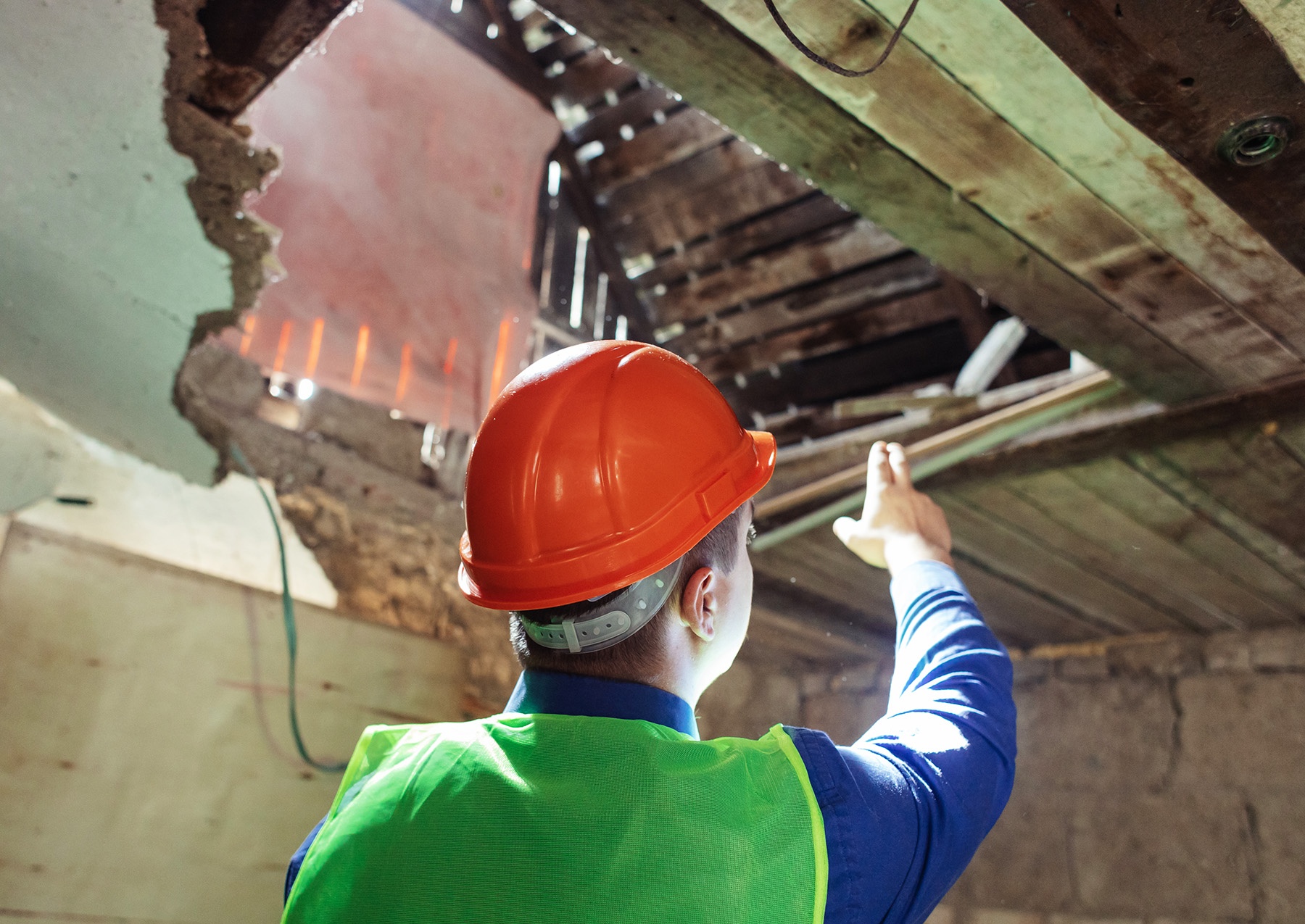 Man wearing safety gear pointing at a hole in a roof