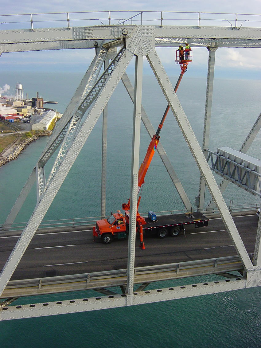 truck on a highway with a crane attached. workers are inspecting a bridge