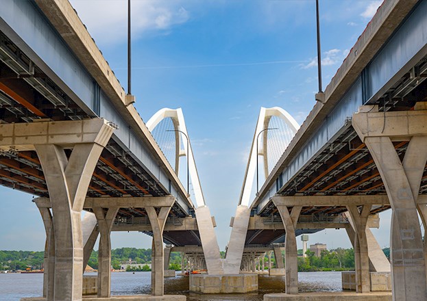 Photo shows the undersides of the twin spans of a bridge, including the piers, foundations, and decks 