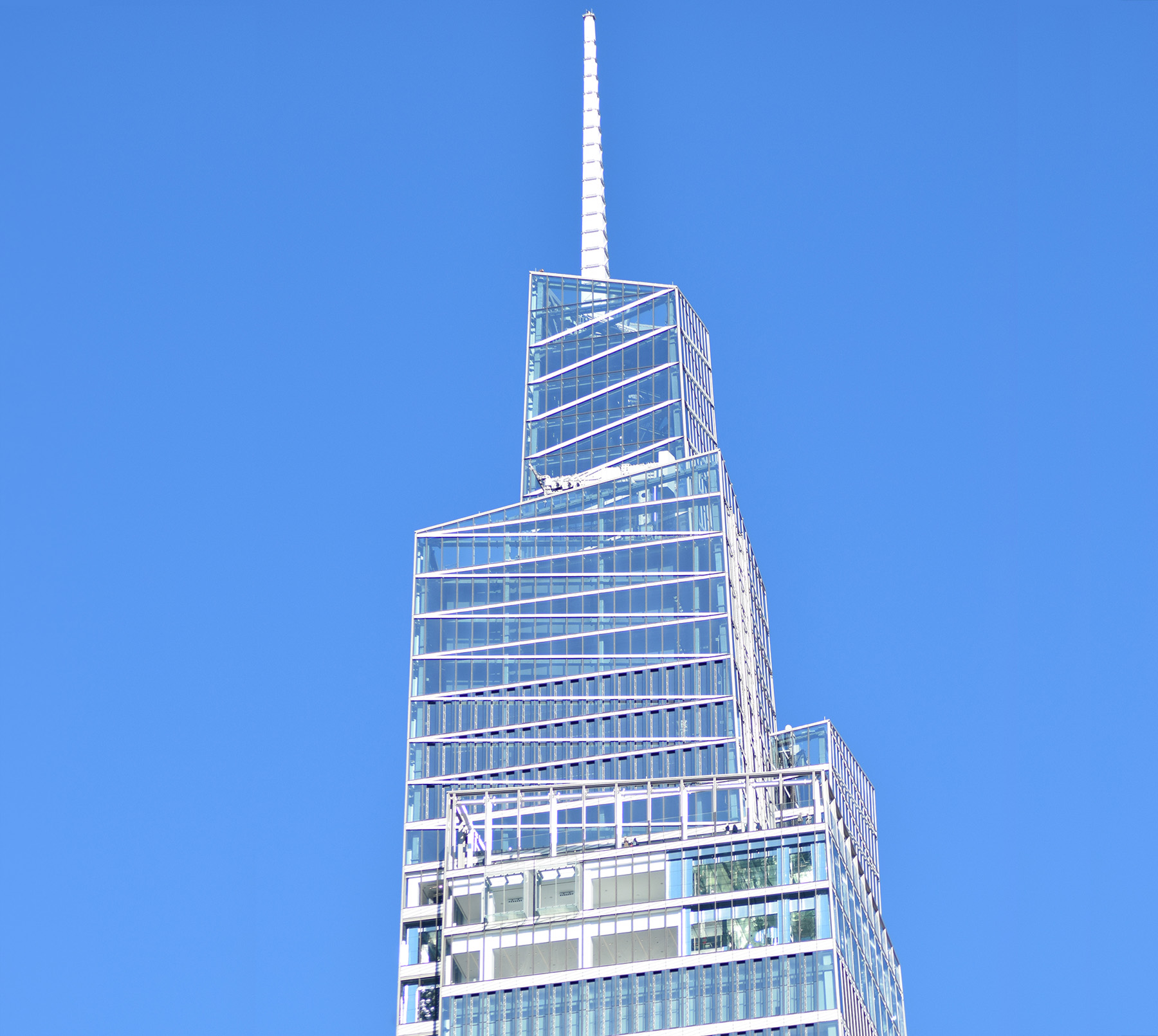 A tall building with stacked, glass volumes. There is a point at the top of the building.