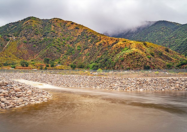 A large hill is in the background and in the foreground is groundwater flowing over rocks. 