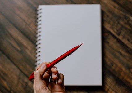 woman holding red pen hovering over blank page
