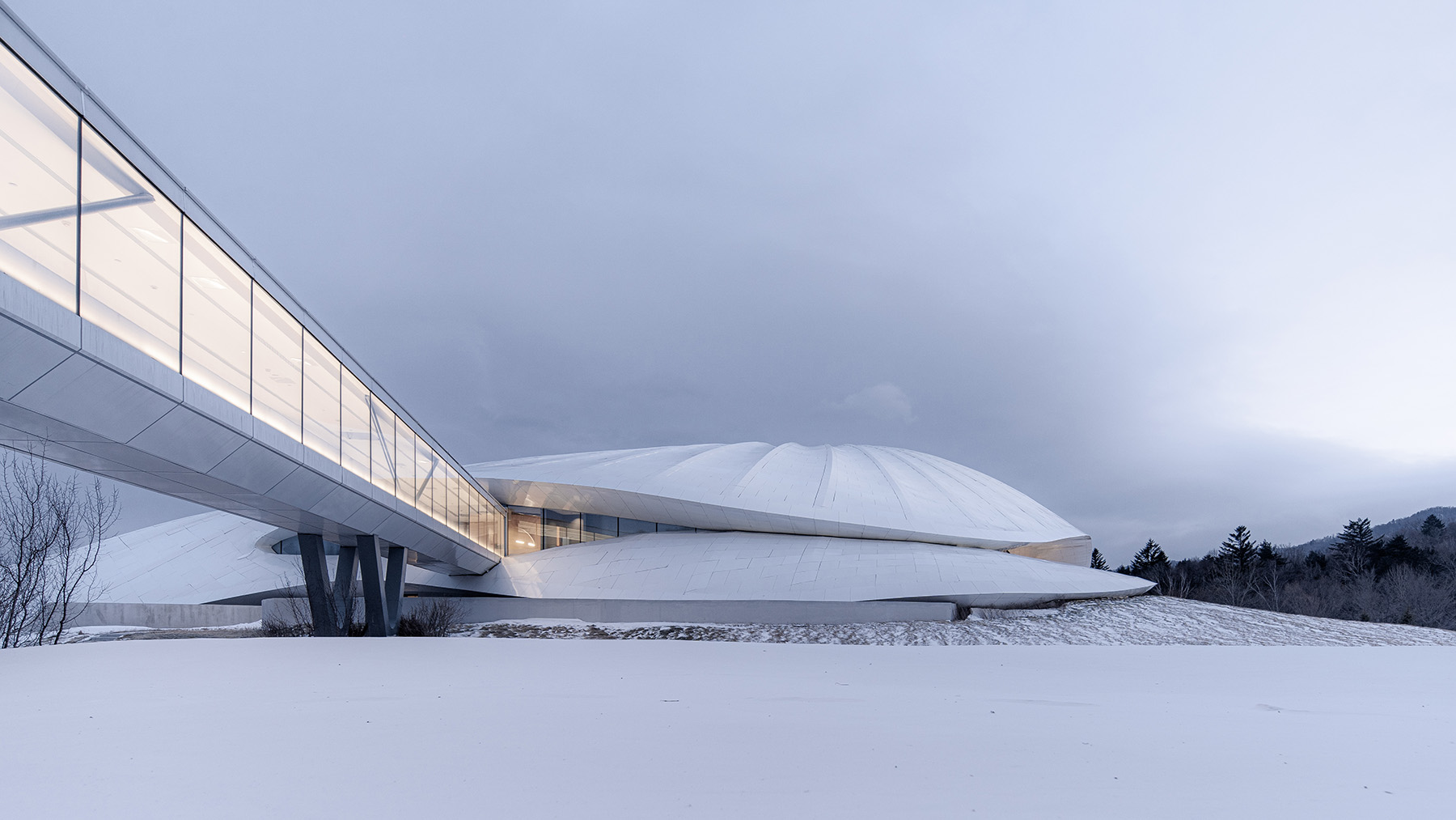 A multistory free-form structure sitting on snow. There is a walkway leading into the building. 