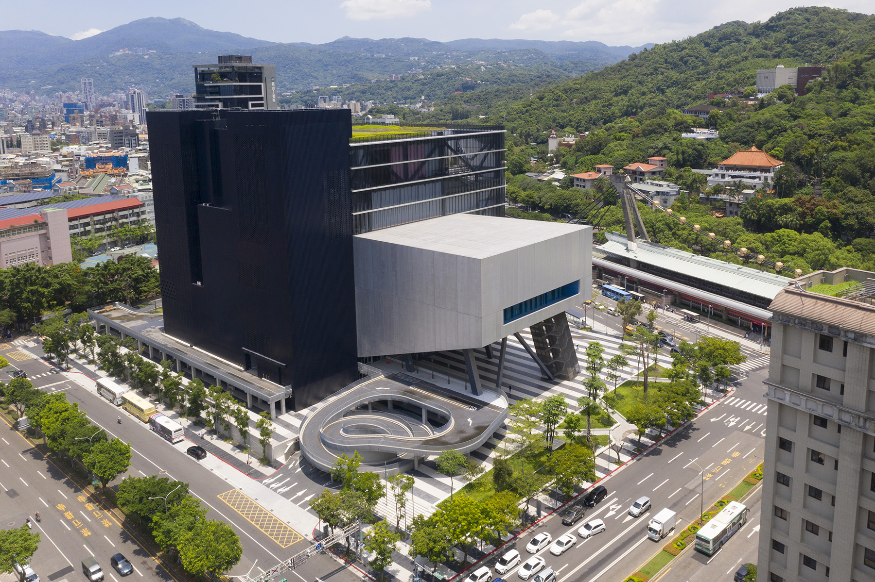 Four-sided building with different shapes projecting from it on one side and four black towers on another side. 