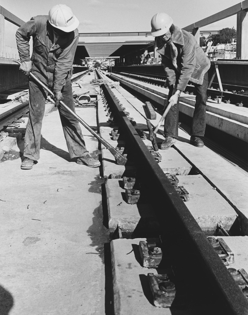 Two workers are helping build train tracks. 