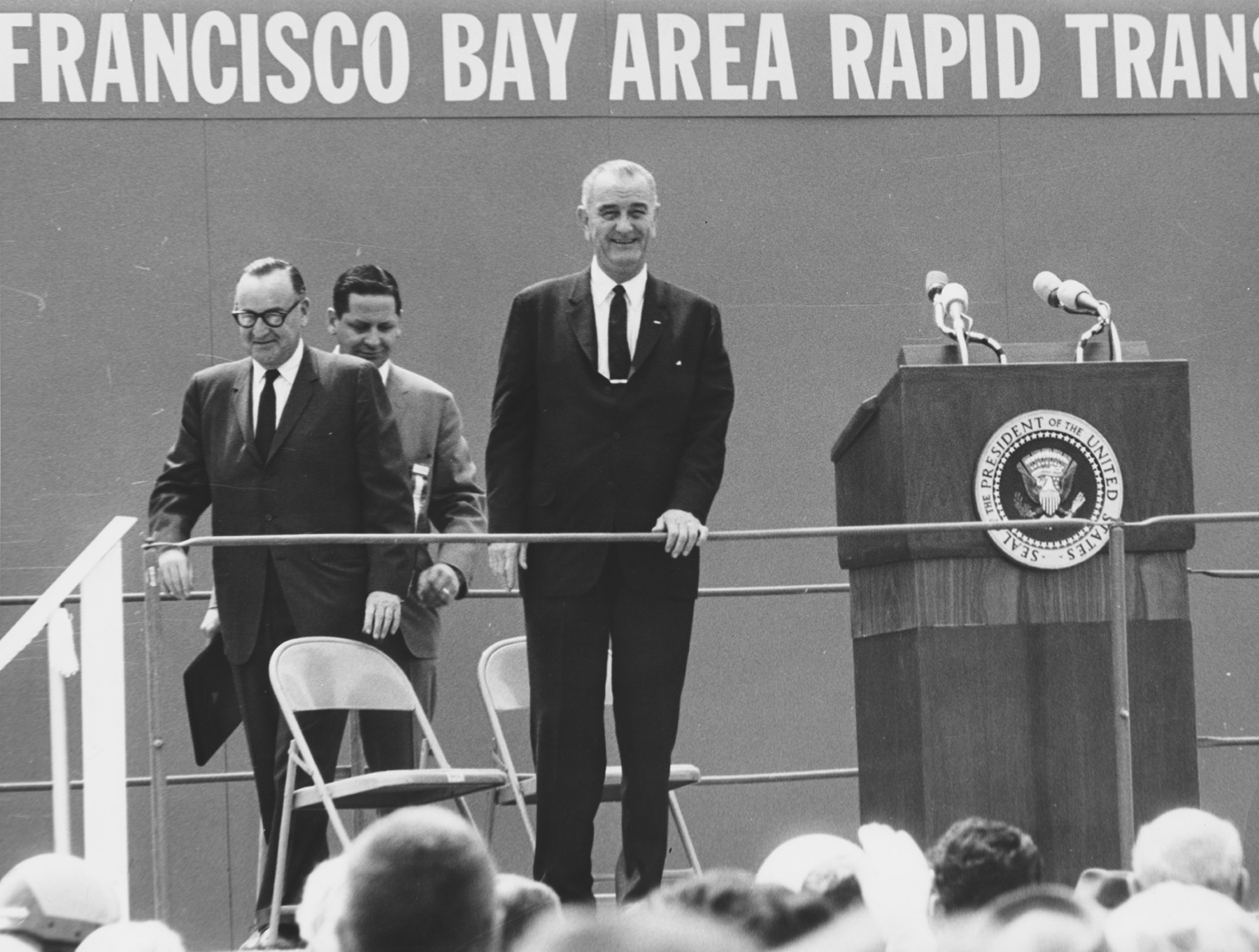 Three men in suits on a dais. 