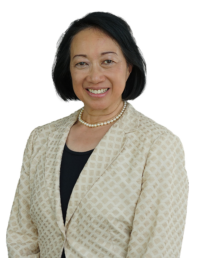 Woman in gold jacket over a black sweater. She is wearing pearls.