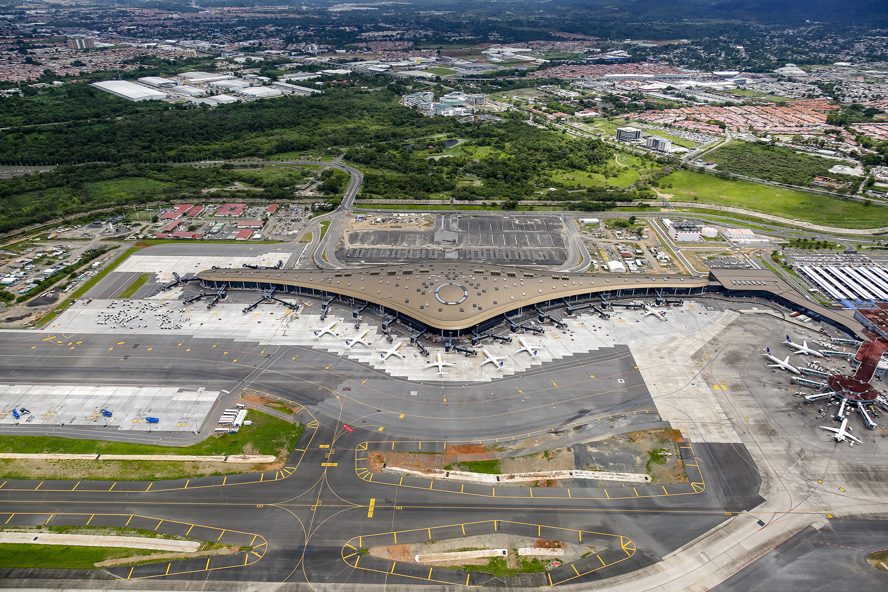 Image shows an airport terminal that is shaped like an aircraft ring. There are many planes parked around the terminal. 