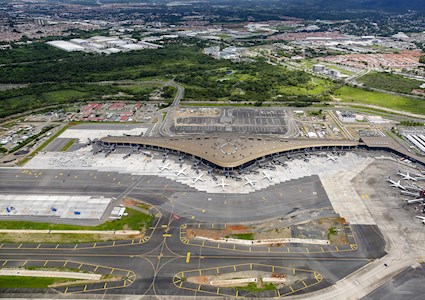 Image shows an airport terminal that is shaped like an aircraft ring. There are many planes parked around the terminal.