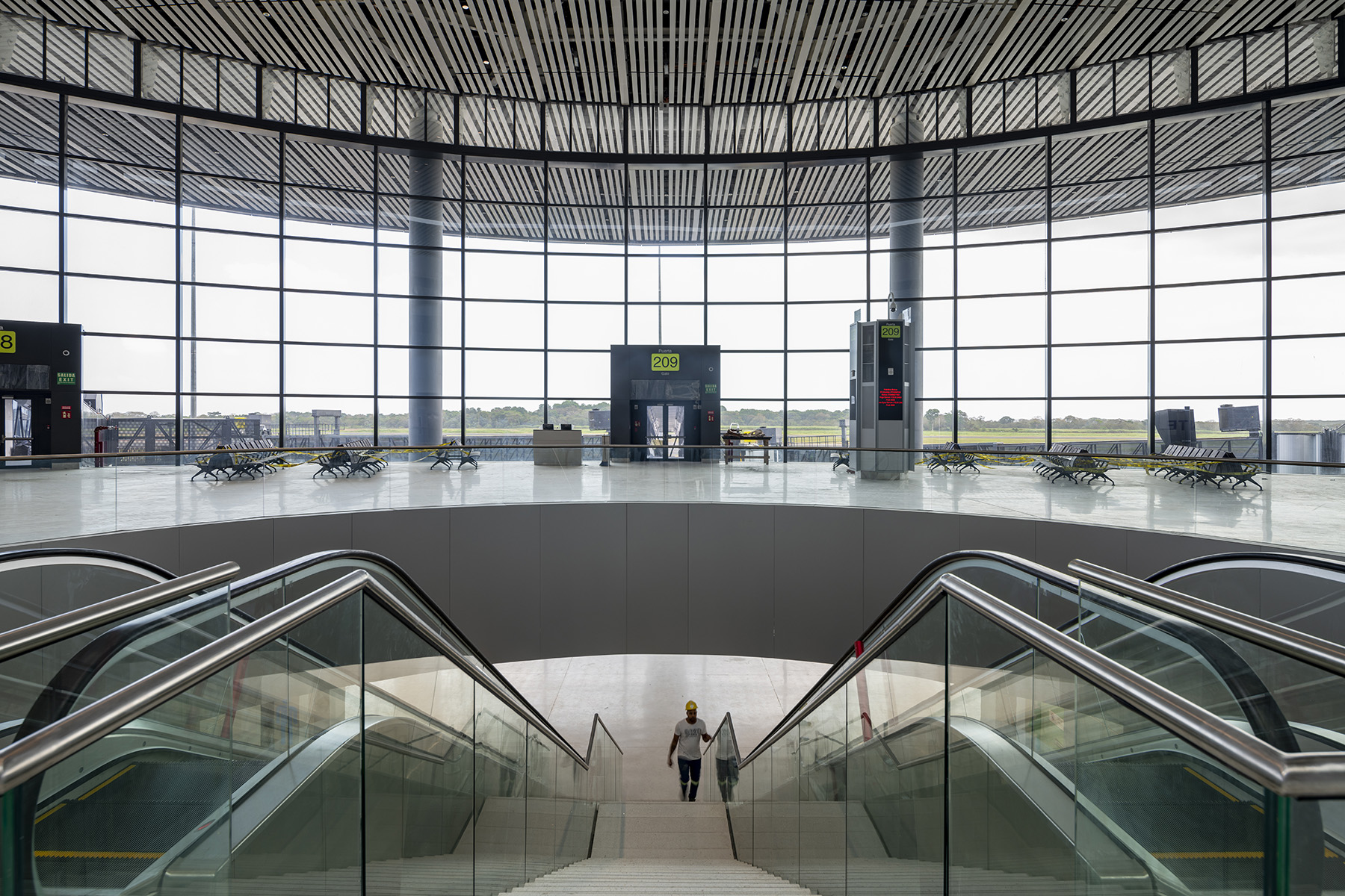 A man walks up stairs inside an airport terminal. On either side of him are escalators.