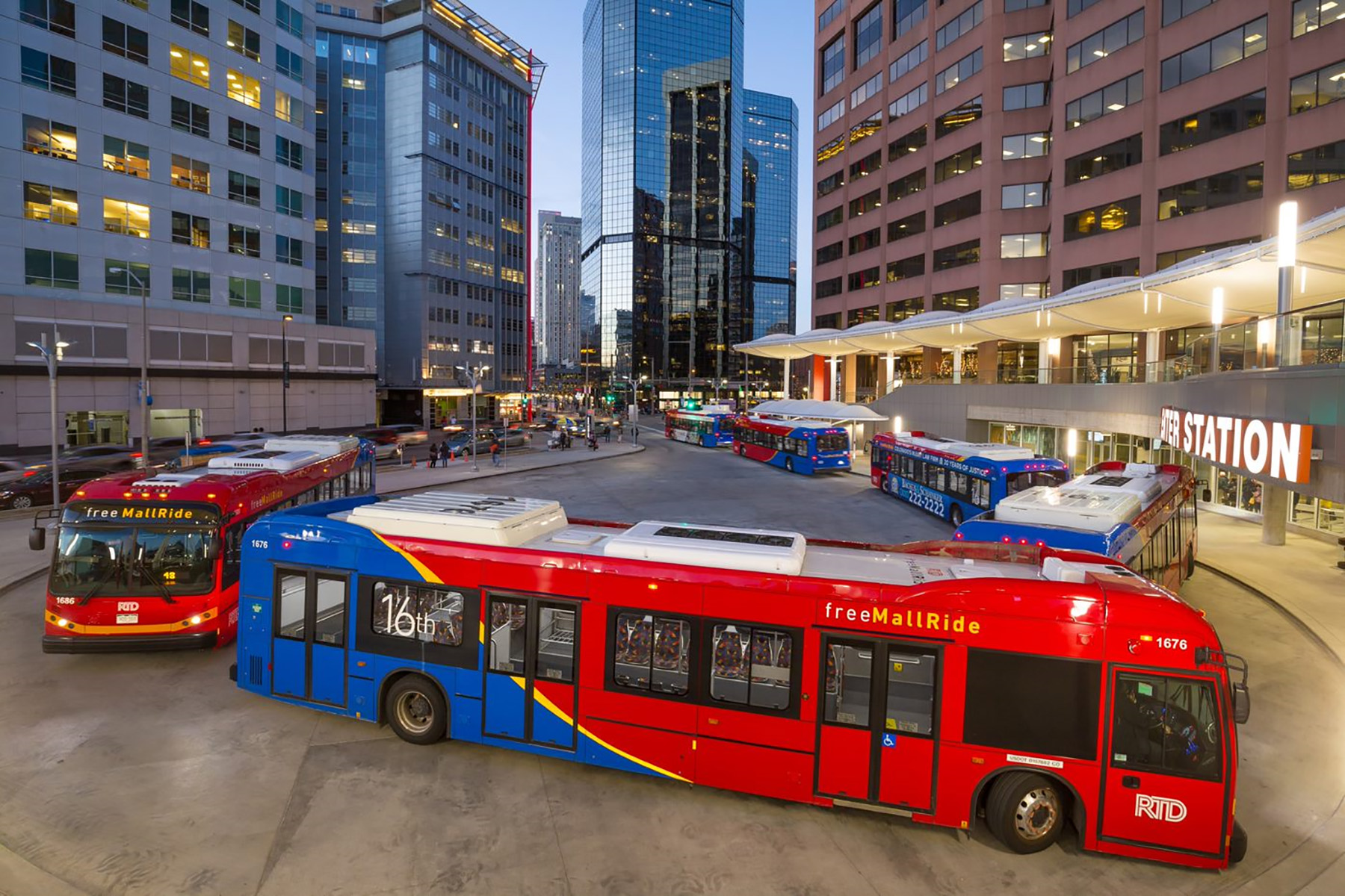 Two red and blue buses leaving a station.