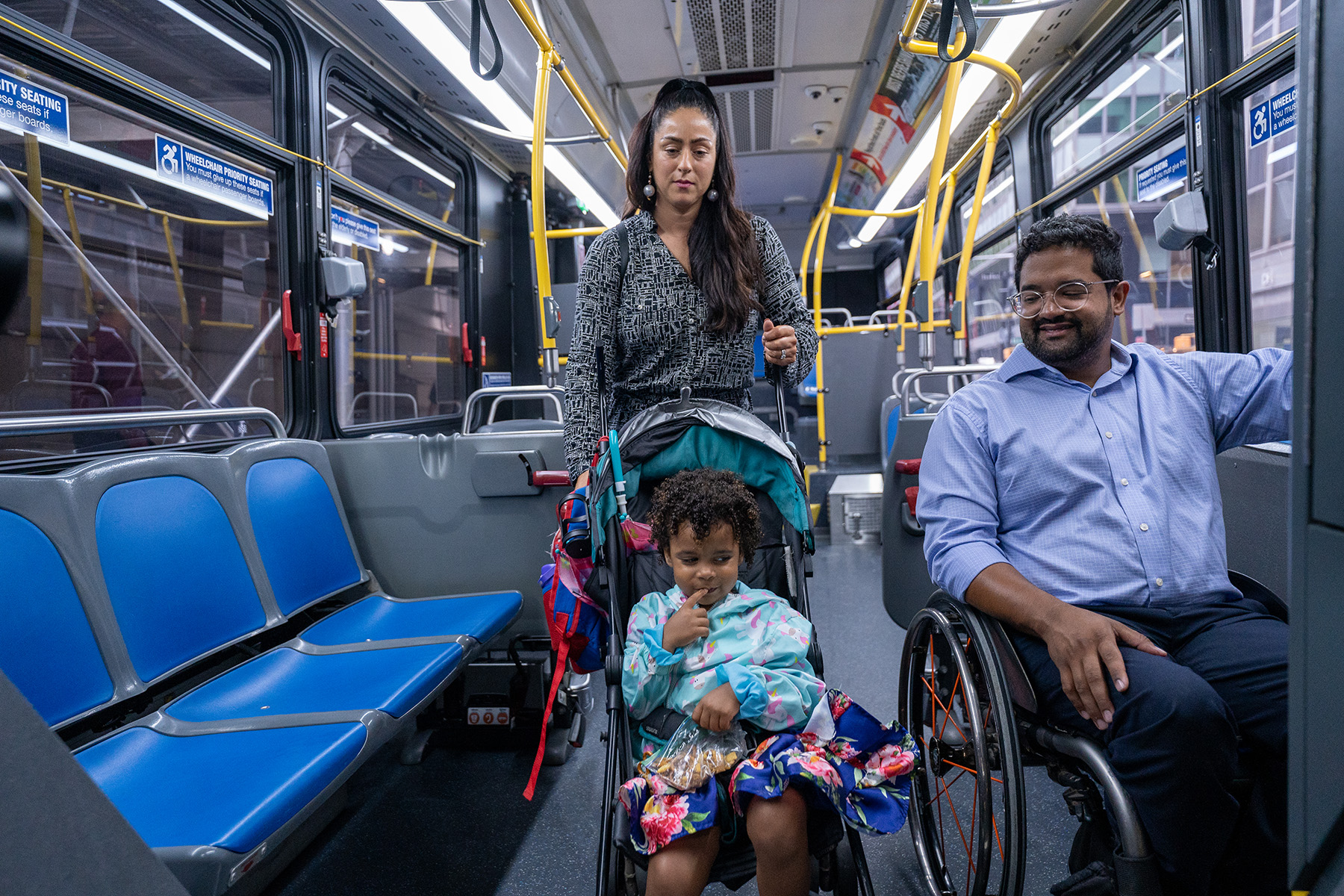 Man in wheelchair and mother and her child are in a bus taking a ride.