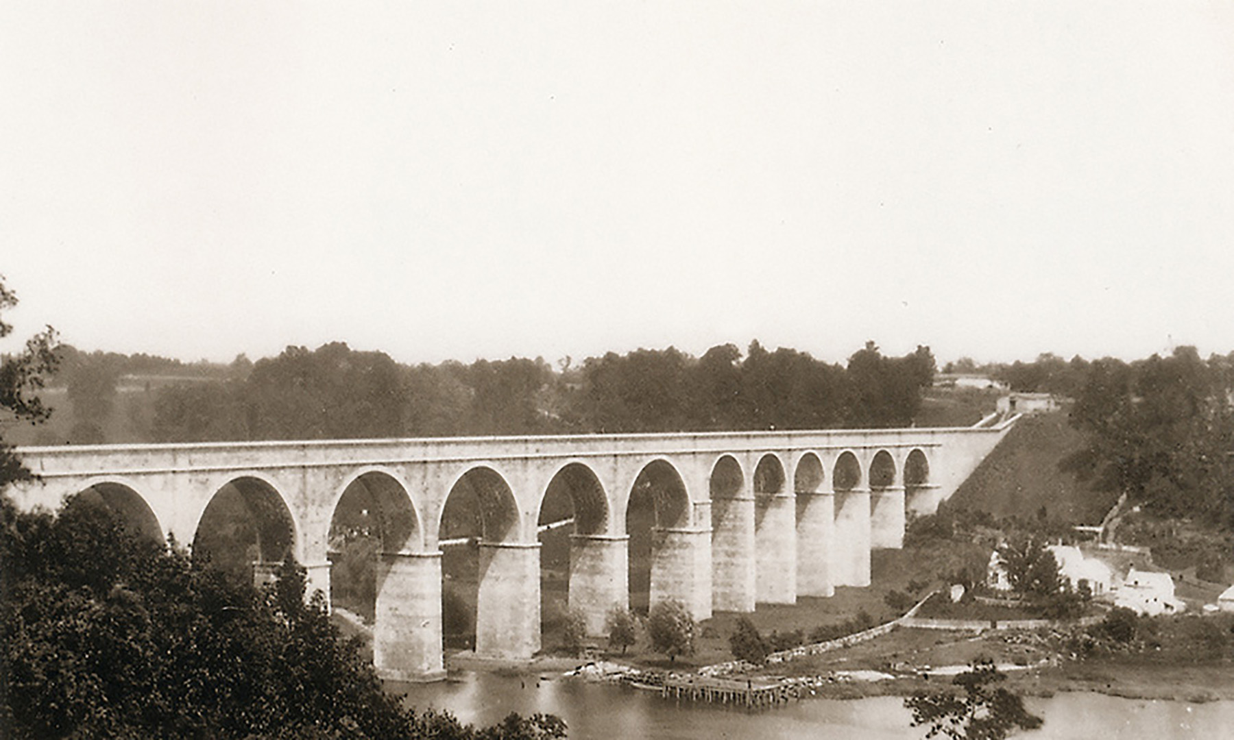 Photograph shows a long, arched structure that spans a river.