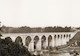 Photograph shows a long, arched structure that spans a river.