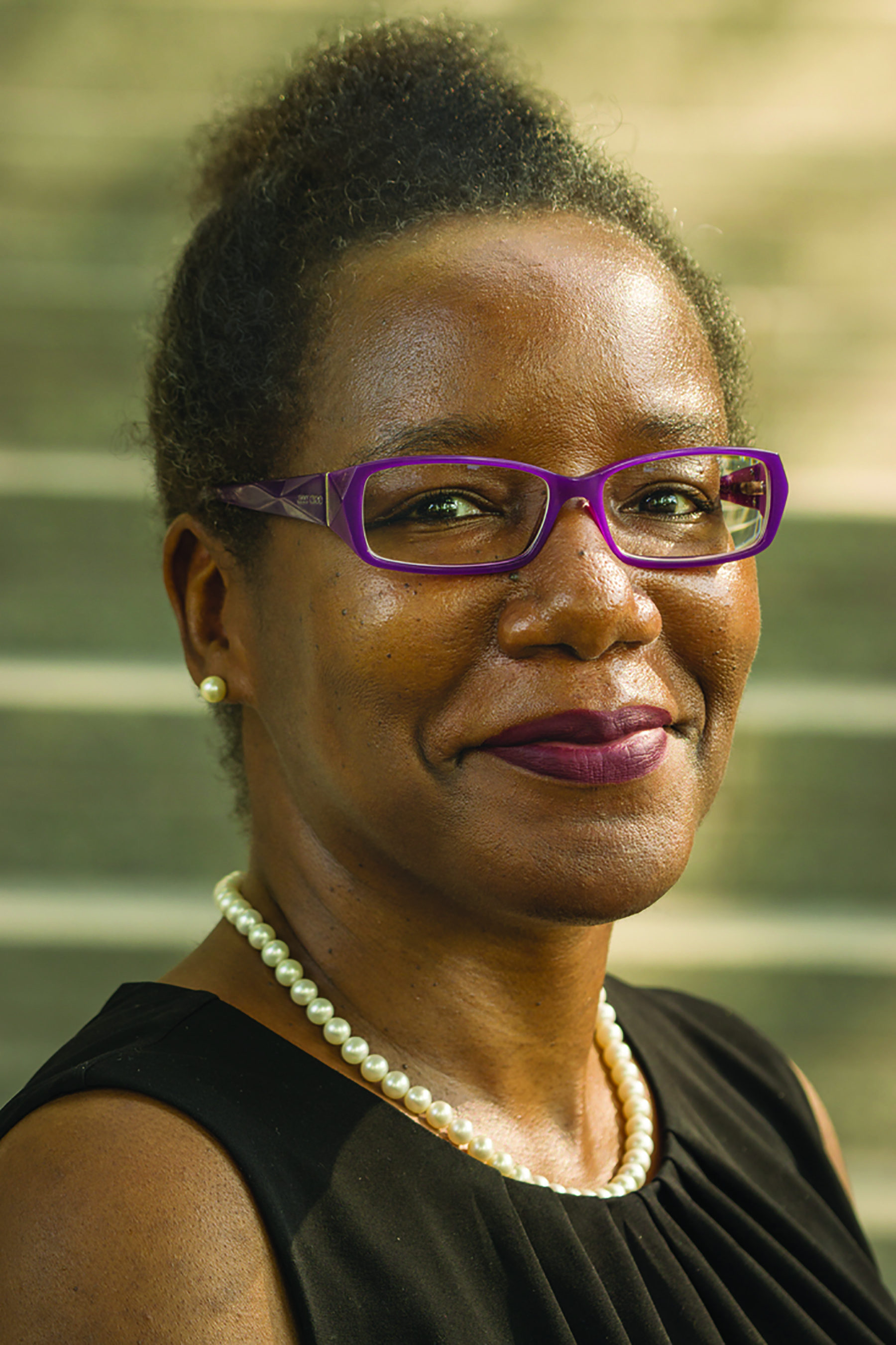 Woman with brown skin in a black sleeveless shirt smiles at the camera.