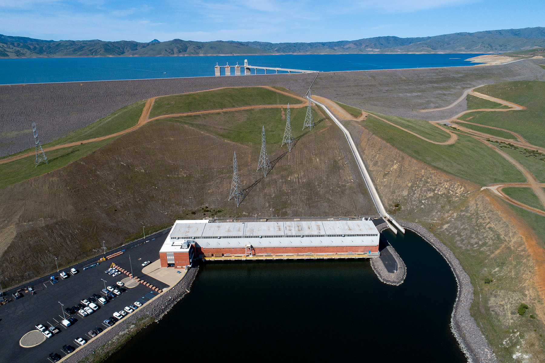 Image shows a dam with two large bodies of water separated by rocks and land. A rectangular building sits next to one of the bodies of water.