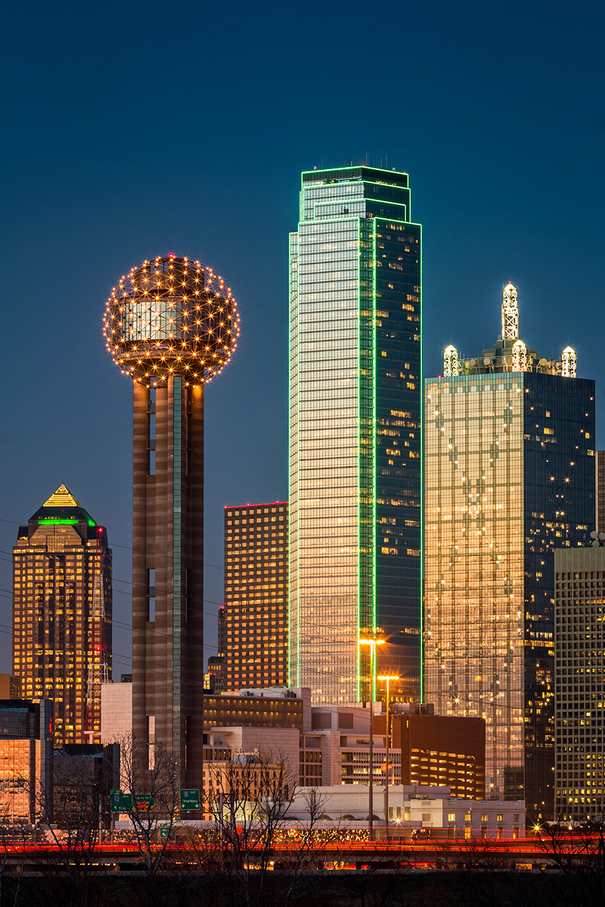 Skyline of the Dallas-Fort Worth area. There are buildings of various sizes lit up at night.