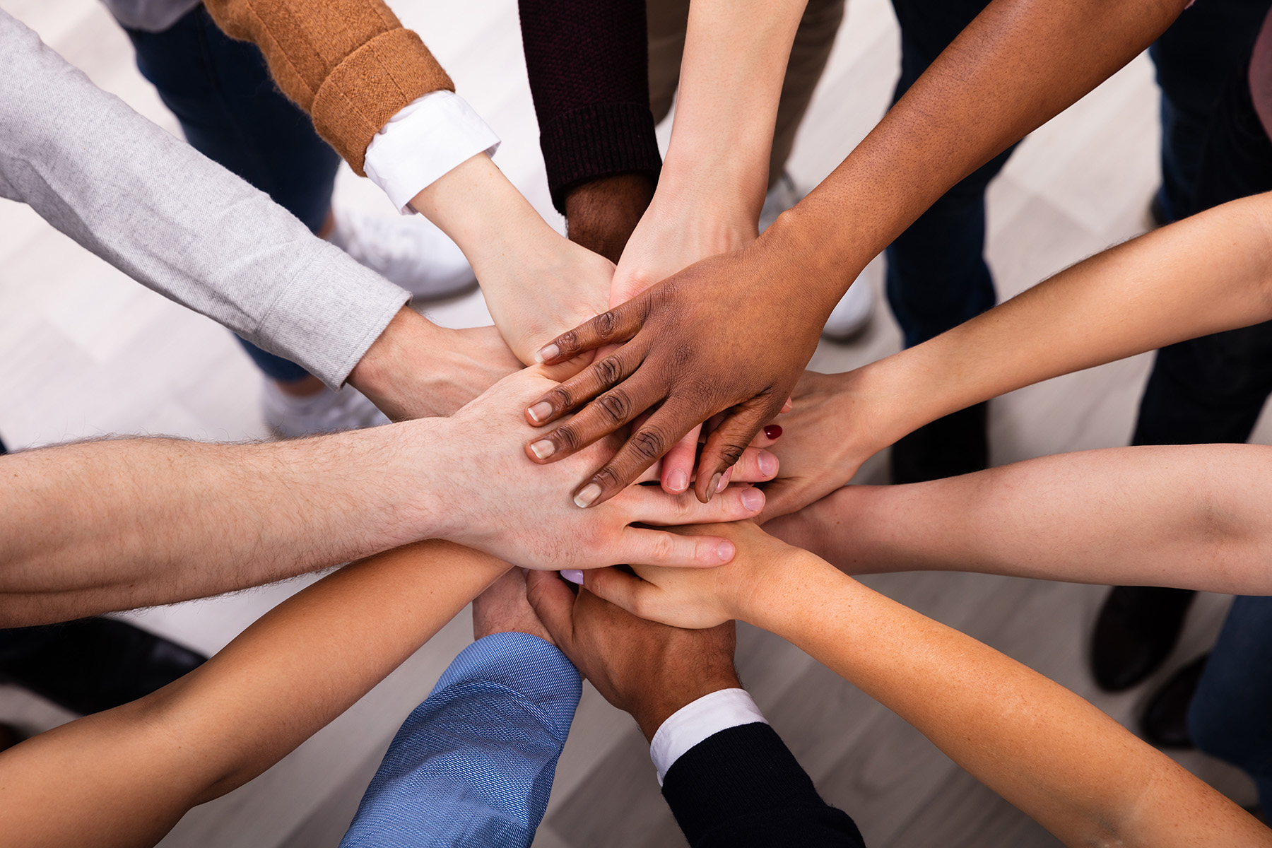 People of various skin tones stretch out their arms and place their hands on top of one another.