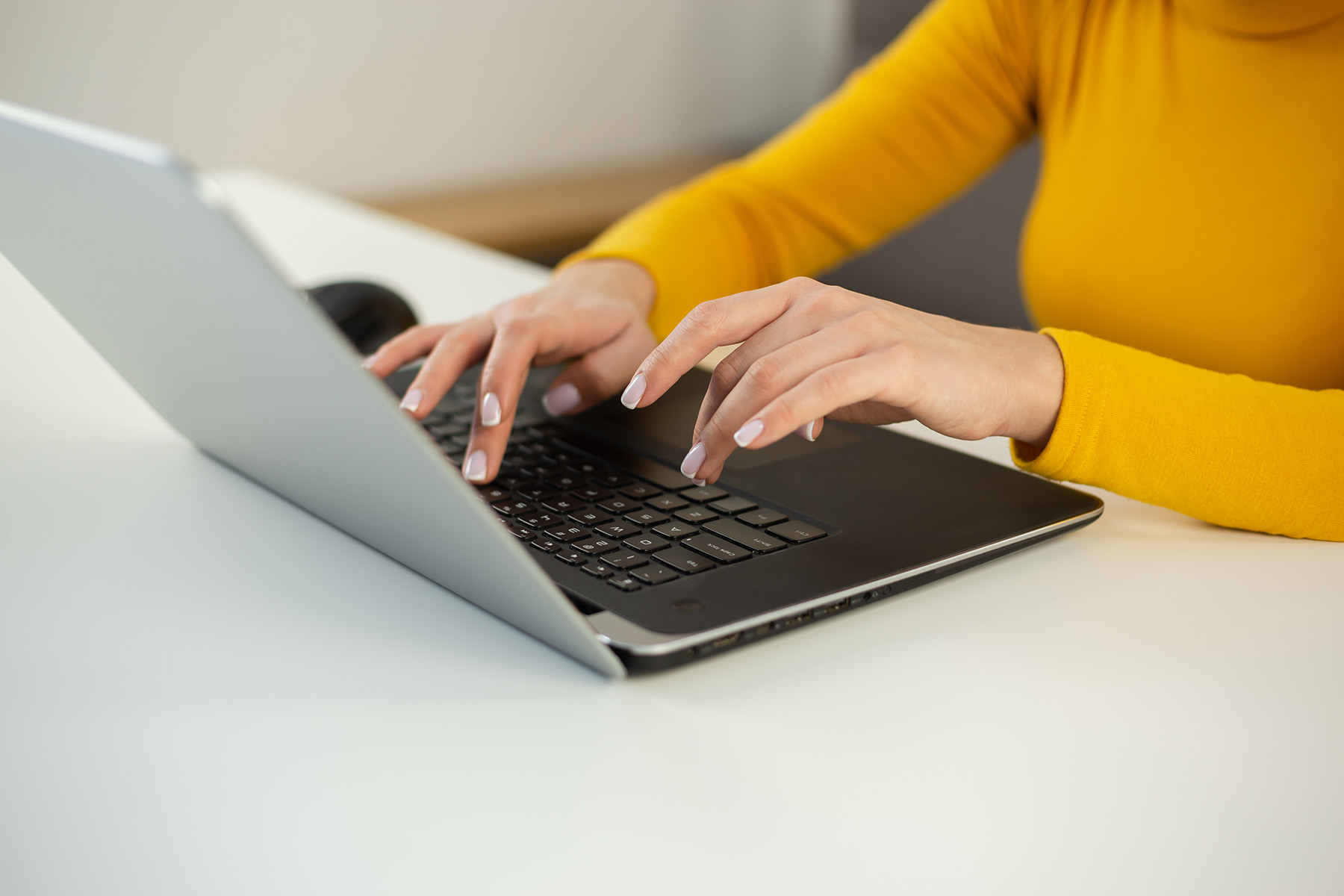 A woman with a gold sweater on types on a laptop. 