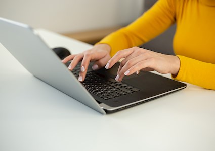 A woman with a gold sweater on types on a laptop. 