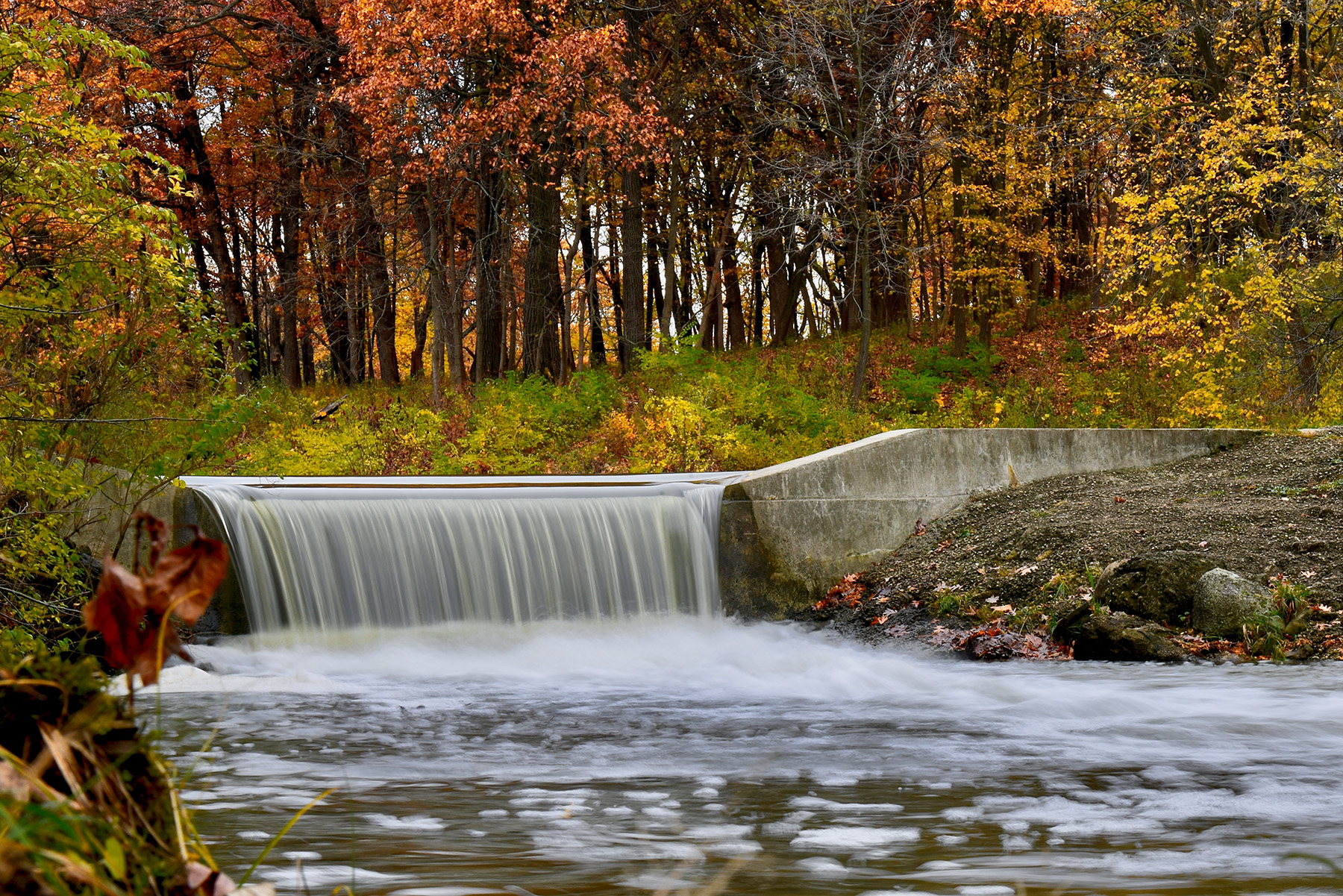 A small waterfall is shown. There are trees with yellow, orange, and green leaves in the background.