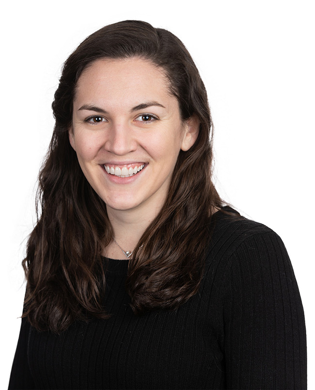 Woman with long brown hair wearing a black sweater smiles at the camera.