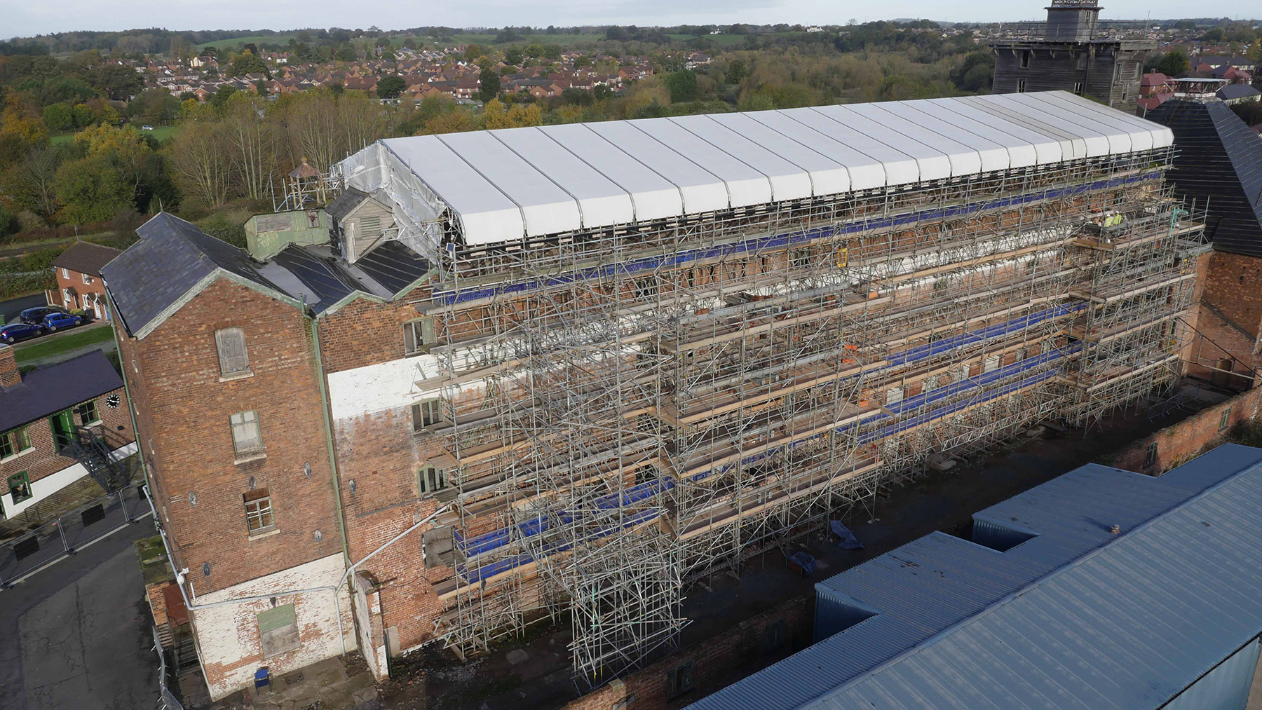 Multistory brick building is surrounded by scaffolding. The roof is gone and in its place is a white tarp.