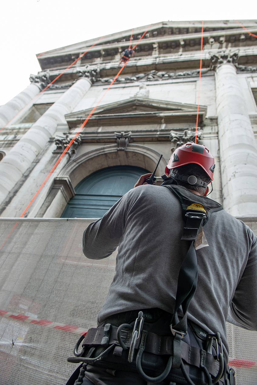 Workers in hard hats and harnesses scale the facade of a building.