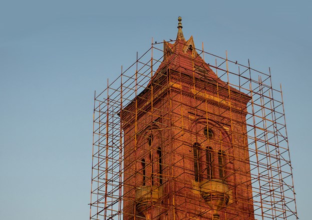 Tall, red brick tower is surrounded by scaffolding.