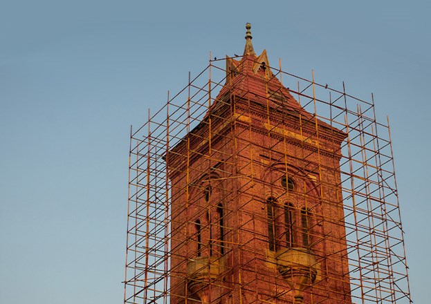 Tall, red brick tower is surrounded by scaffolding. 
