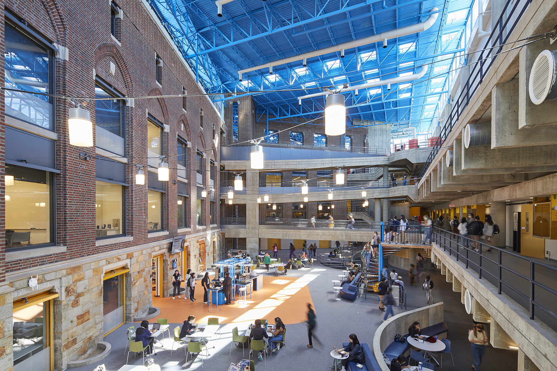 A large, open, multistory space with enclosed walls and elevated walkways. There are many women walking around, seated, and standing within the space. 