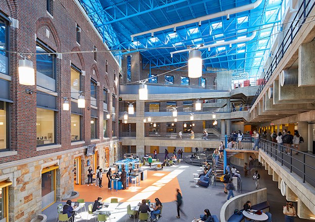 A large, open, multistory space with enclosed walls and elevated walkways. There are many women walking around, seated, and standing within the space.