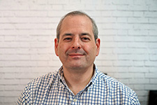 man in white and blue checked shirt smiles at the camera.